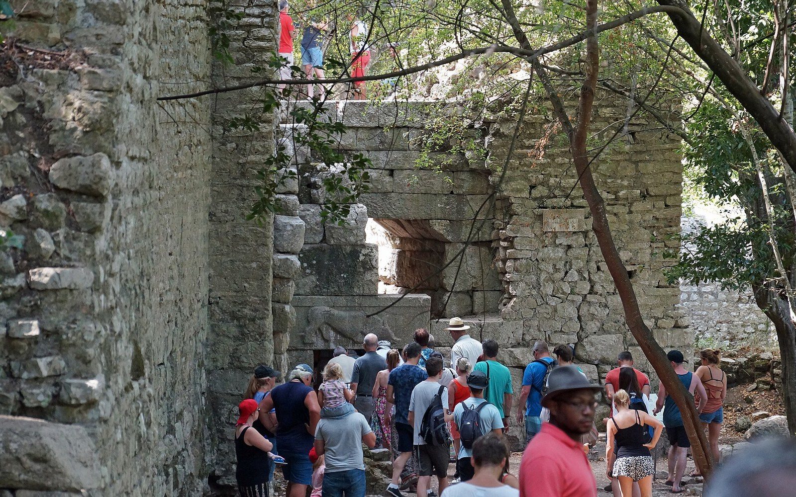 Visitors gathered at a stone gateway with a carved lion relief above the lintel