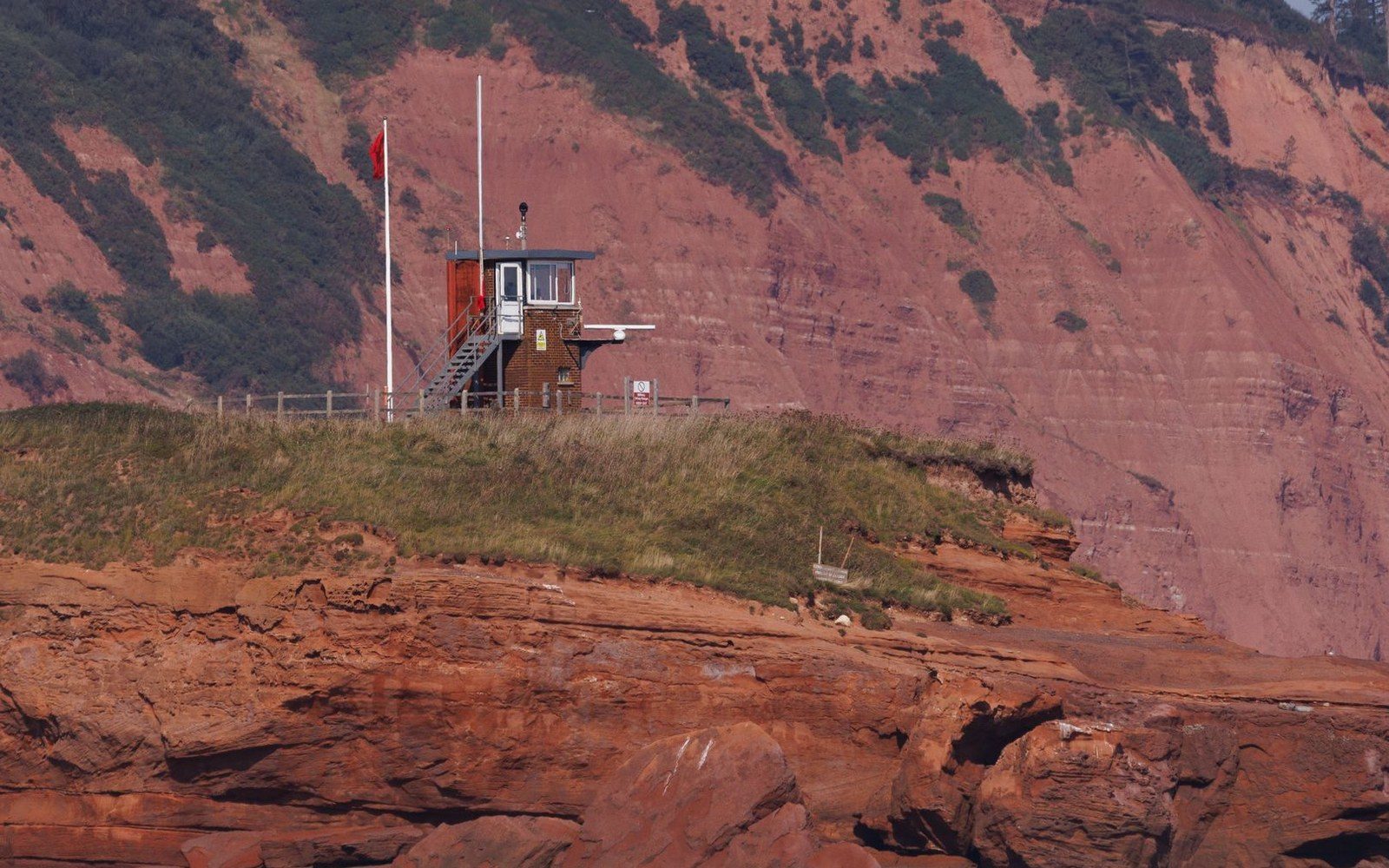 A small lookout station on a grassy clifftop above red sandstone cliffs